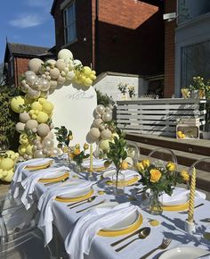 a table set up with yellow and white plates, silverware and balloons in the air