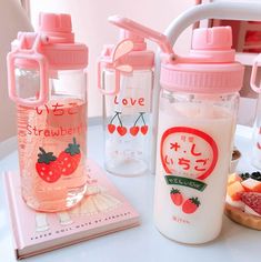 two water bottles with strawberries on them sitting next to a book and other items