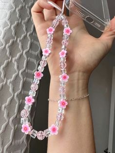 a person holding up a cell phone with pink flowers on it's chain attached to their wrist