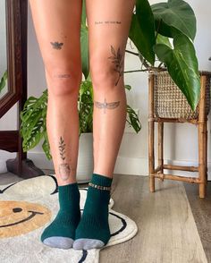 the legs of a woman with tattoos on them are standing in front of a potted plant