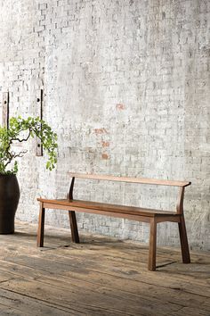 a wooden bench sitting next to a potted plant on top of a hard wood floor