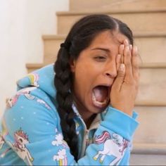 a woman with her mouth open and holding her hands to her face while sitting on the stairs