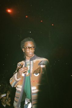 a man standing in front of a crowd at a concert wearing a jacket and sunglasses