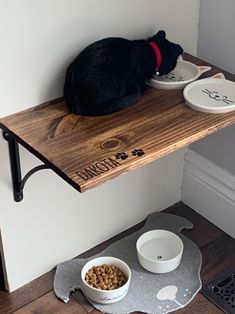 a cat sitting on top of a wooden shelf next to two bowls with food in them