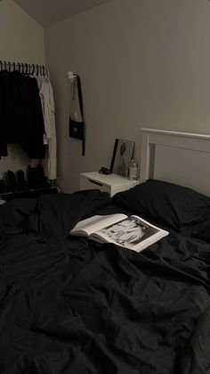 an unmade bed in a bedroom with black sheets and clothes hanging on the wall