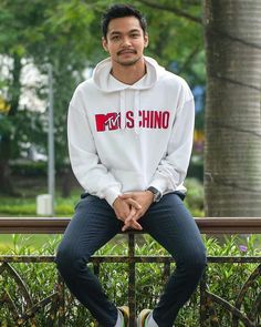 a man sitting on top of a bench wearing a white hoodie and blue jeans