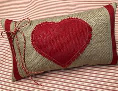 a pillow with a heart on it sitting on top of a striped bed sheet,