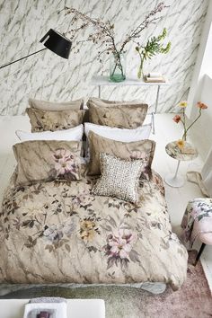 a bed with floral comforter and pillows in a white room next to a lamp