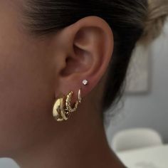 a close up of a woman's ear wearing gold hoops and diamond earrings