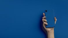 a person holding up a blue phone in front of a blue wall with their hand on it