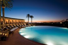 an outdoor swimming pool with chaise lounges and palm trees in the background at night