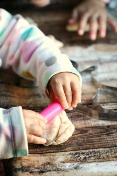 a small child is playing with dough on the table and holding a pink object in their hand