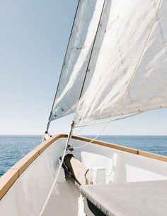 there is a sailboat with white sails on the open water and blue sky in the background