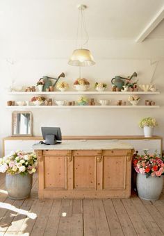 a wooden table topped with lots of vases filled with flowers next to a wall mounted shelf