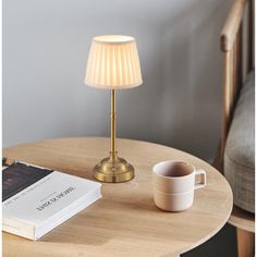 a table with a lamp, coffee cup and book on it next to a chair