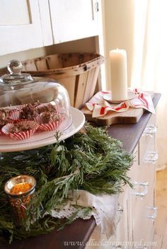 a table topped with a cake covered in frosting and christmas greenery next to a candle