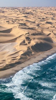 an aerial view of the ocean and sand dunes in the desert, with waves crashing on the beach