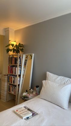 a bed with white sheets and pillows next to a bookshelf filled with books