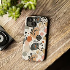 an iphone case sitting on top of a wooden table next to a camera and plant