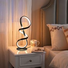 a night stand with a lamp on it next to a bed