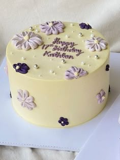 a yellow birthday cake with purple flowers on it