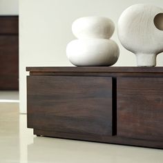 two white vases sitting on top of a wooden cabinet