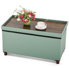 a green box with some flowers and a cup on the top is sitting on a table