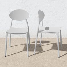 two white chairs sitting next to each other on top of a cement floor in front of a white wall