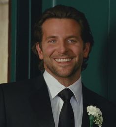 a man in a suit and tie smiles at the camera while wearing a boutonniere