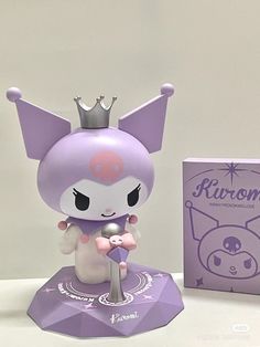 a purple figurine with a silver crown on it's head next to a box