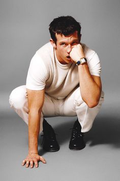 a man kneeling down with his hand on his face while wearing white pants and black shoes