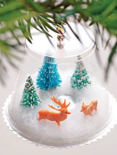 a christmas ornament hanging from a tree branch with two deer and pine trees in it