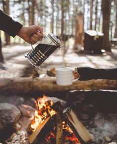 two people are toasting over a campfire with coffee mugs in their hands