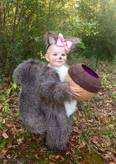 a baby dressed up as a squirrel holding an egg in its arms and wearing a bunny costume