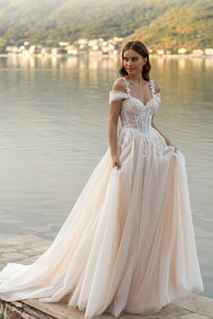 a woman in a wedding dress standing on the edge of a body of water with her hand on her hip