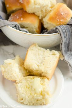 several rolls are on a plate next to a bowl of buttered rolls and a napkin