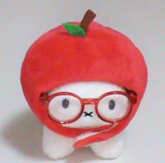 a stuffed animal with glasses and a red apple on it's head, sitting in front of a white background