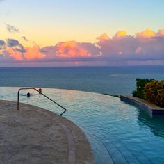 an empty swimming pool in front of the ocean at sunset with clouds and blue sky