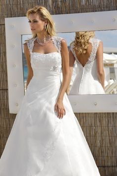 a woman in a white wedding dress standing next to a mirror with her reflection on it