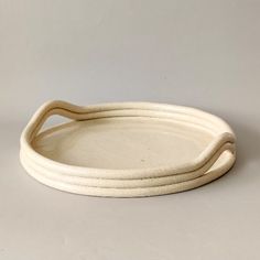 two white oval serving trays sitting on top of each other, one with curved handles