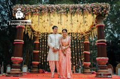 a man and woman standing in front of a decorated stage with flowers on the side