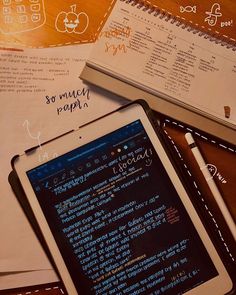 a tablet computer sitting on top of a wooden table next to notebooks and papers