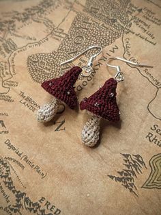 two crocheted gnome hats are hanging from silver earwires on a map