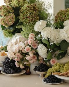 a table topped with plates filled with fruit and flowers next to vases full of flowers