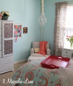 a bedroom decorated in blue and pink with a bed, chair, dresser and window