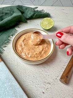 a hand holding a spoon over a bowl of peanut butter with limes on the side