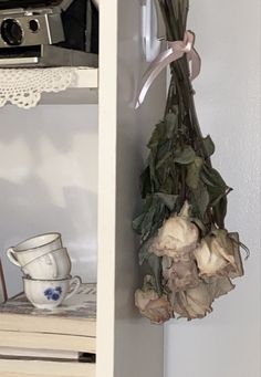 a bunch of dried flowers hanging from a shelf next to a cup and saucer