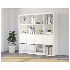 a white bookcase filled with books next to a potted plant