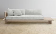 a couch sitting on top of a wooden floor next to a white wall with three pillows