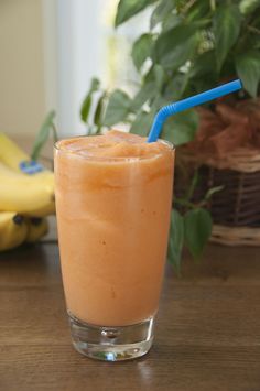 an orange drink with a blue straw sitting on top of a wooden table next to bananas